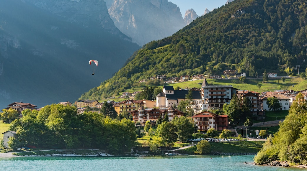 A mountainous landscape with a lake, a town with traditional buildings, and a paraglider in the distance.