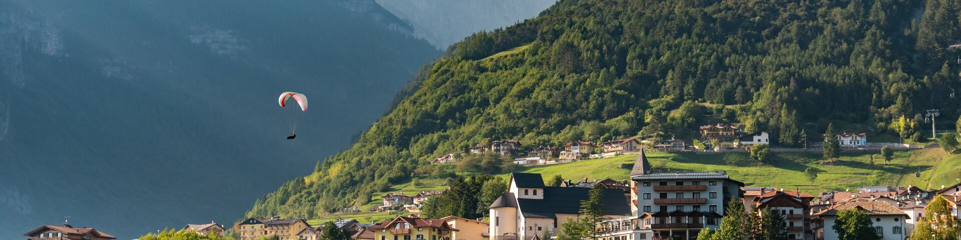 Un paisaje montañoso con un lago, un pueblo con edificios tradicionales y un parapentista a lo lejos.