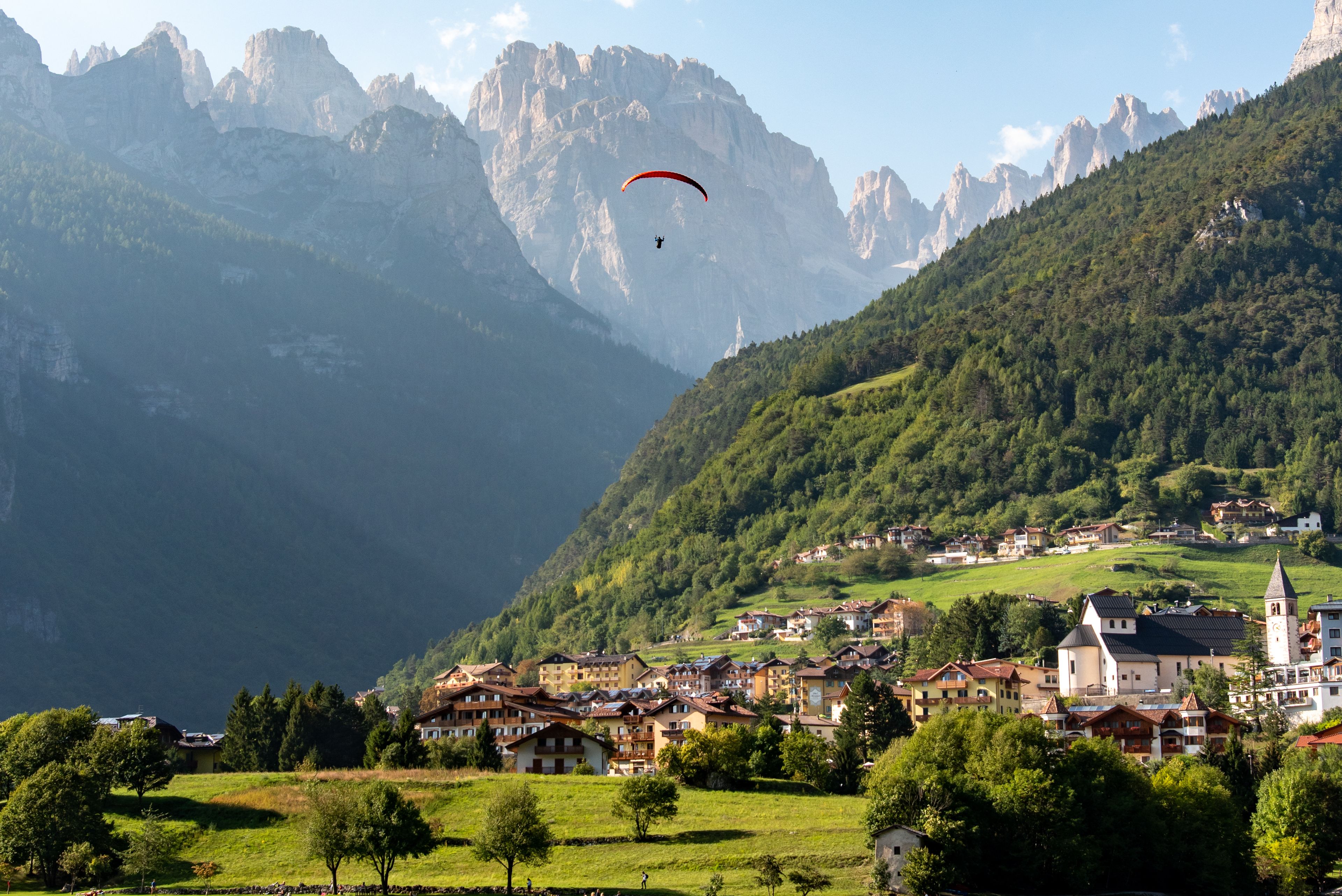 A mountainous landscape with a village, a person paragliding, and a church.