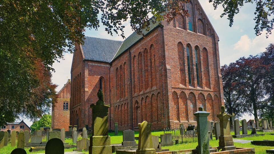 A large brick church with a tall steeple and arched windows, surrounded by a cemetery with headstones.