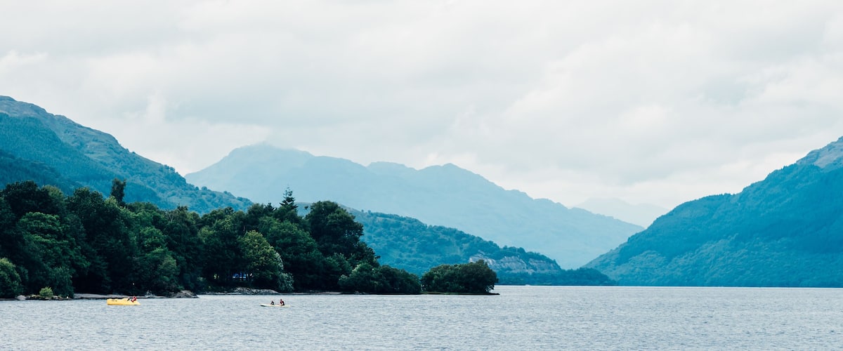 A calm lake surrounded by lush green mountains under a cloudy sky.