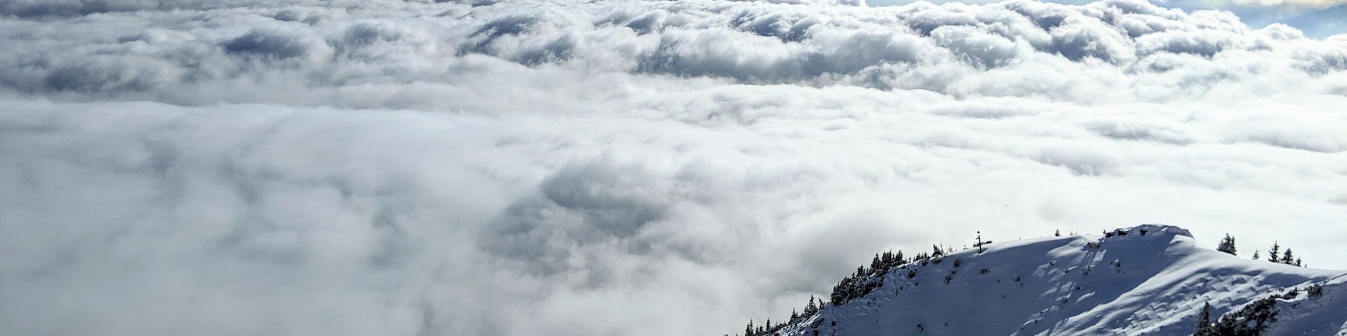 A snow-covered mountain landscape with a ski lift and a view of the clouds below.
