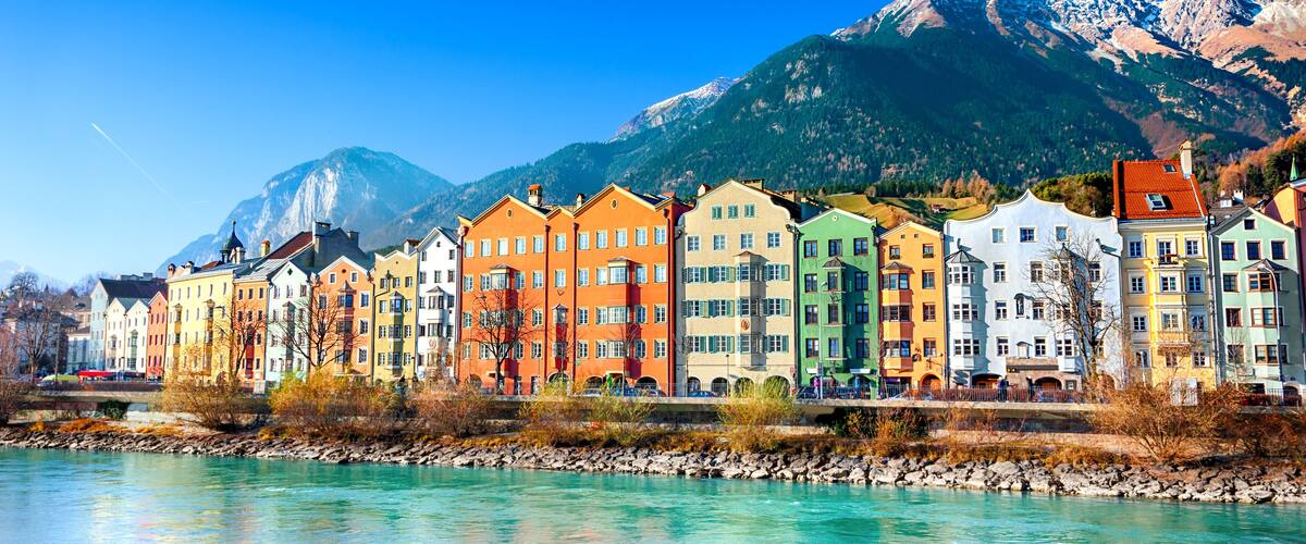 A row of colorful buildings along a river with mountains in the background.