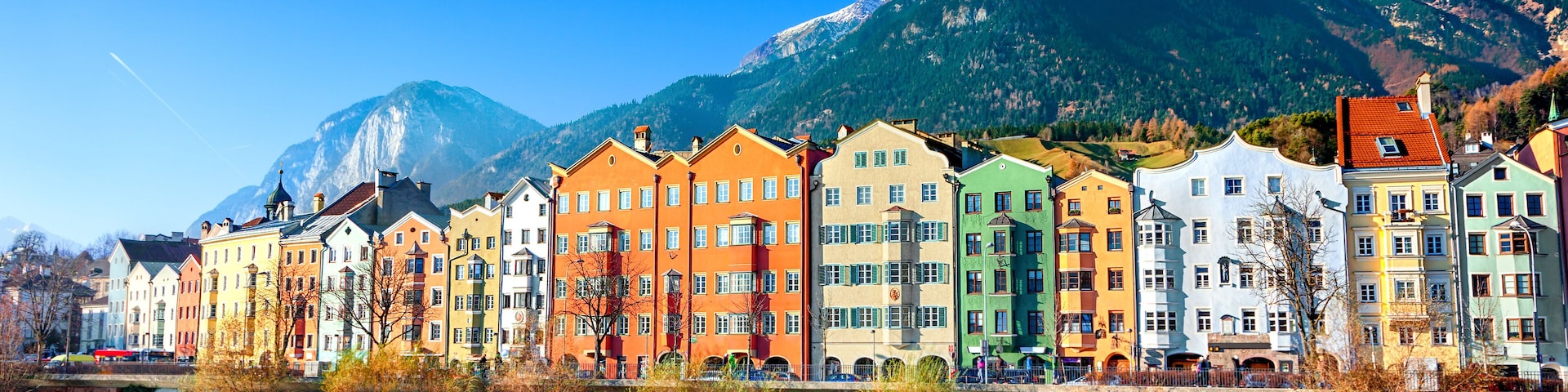 A row of colorful buildings along a river with mountains in the background.