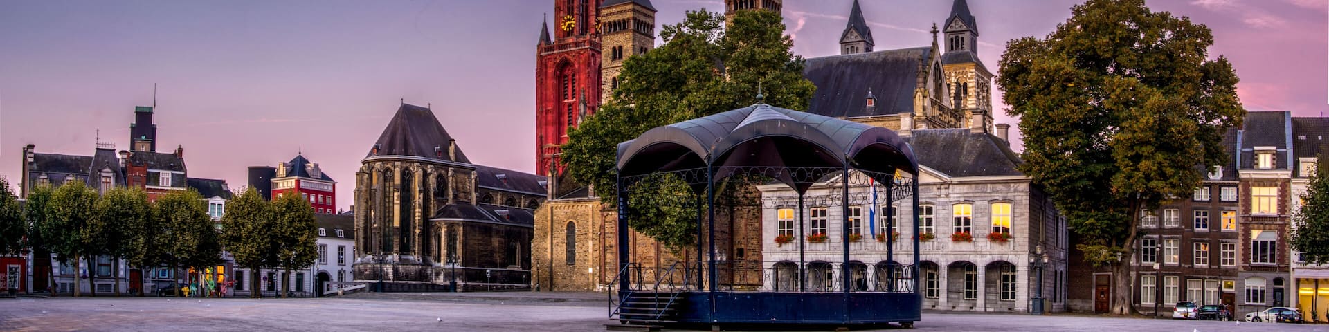 A historic city square with a prominent church, a clock tower, and a covered pavilion.