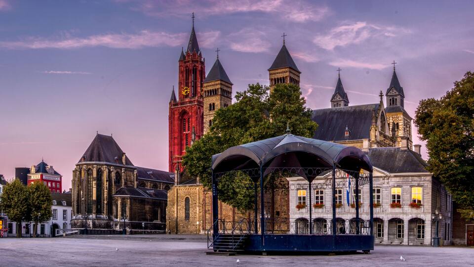 A historic city square with a prominent church, a clock tower, and a covered pavilion.