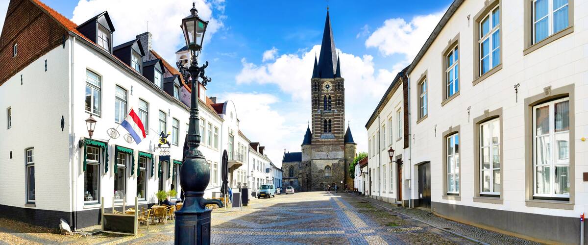 A cobblestone street lined with historic buildings, a prominent church tower, and a traditional street lamp.