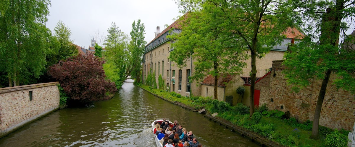 A narrow canal with a boat carrying passengers, surrounded by brick buildings and lush greenery.