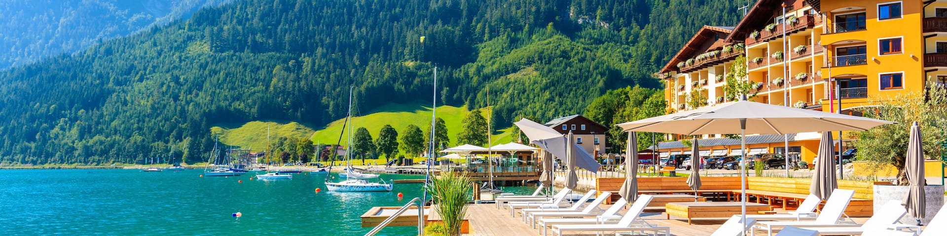 Pier with chairs on sunny terrace on shore of beautiful Achensee lake on sunny summer day with blue sky, Karwendel mountain range, Tirol, Austria