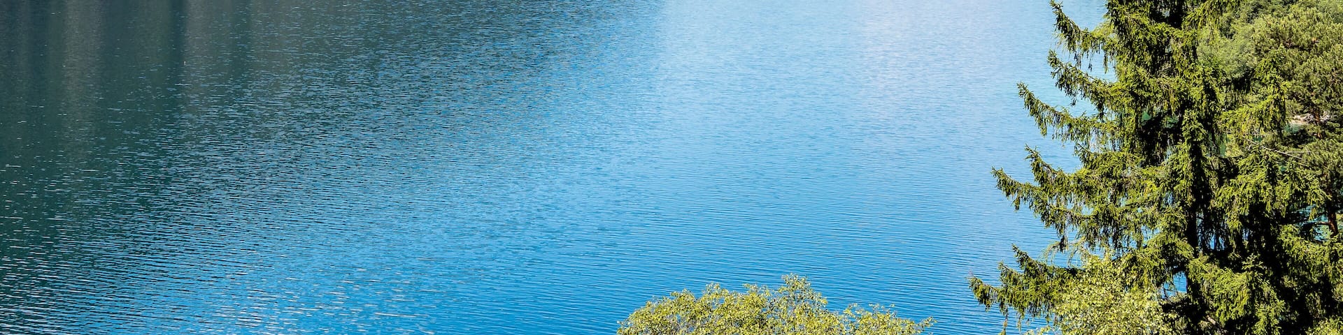A calm lake surrounded by forested mountains under a clear sky.