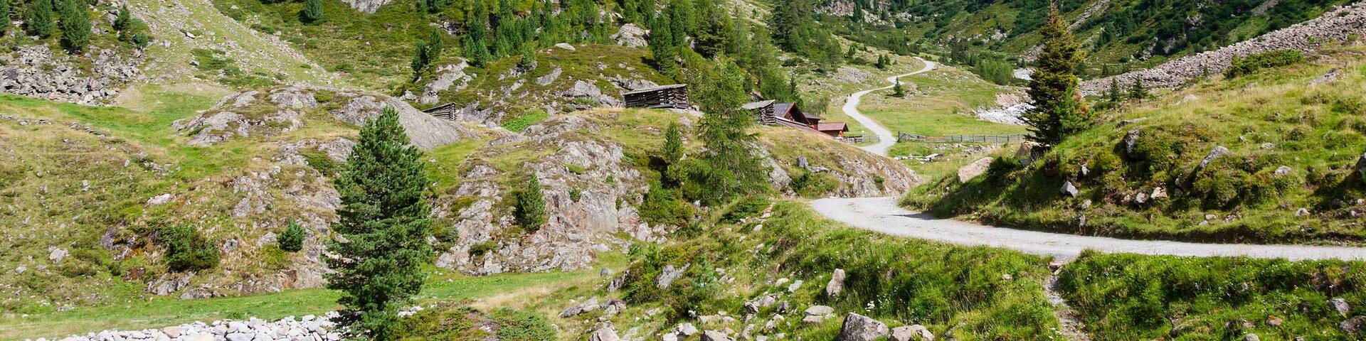 A mountainous landscape with a winding road, a small cabin, and a prominent peak.