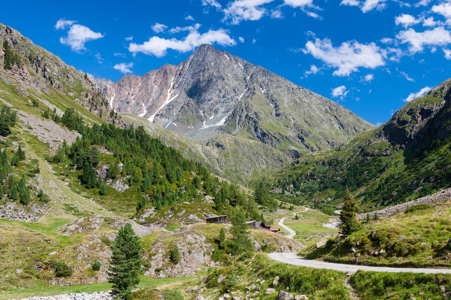 A mountainous landscape with a winding road, a small cabin, and a prominent peak.