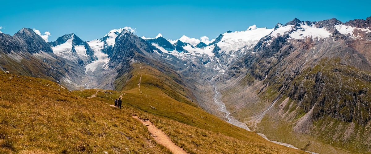 A mountain range with a clear sky, a winding path, and a group of hikers.