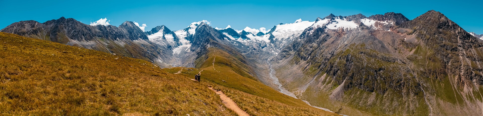 A mountain range with a clear sky, a winding path, and a group of hikers.