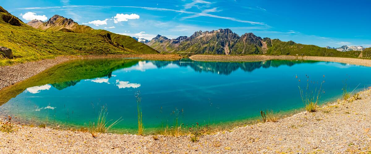 A clear lake surrounded by mountains and a gravel path.