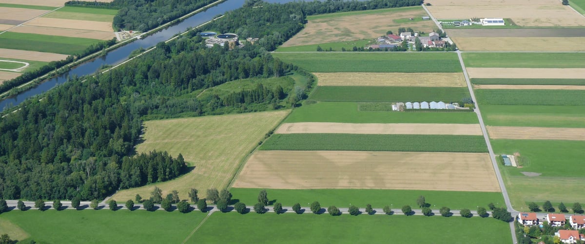 An aerial view of a river winding through a rural landscape with fields, a small town, and a lake.