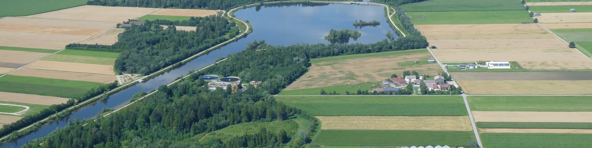 An aerial view of a river winding through a rural landscape with fields, a small town, and a lake.