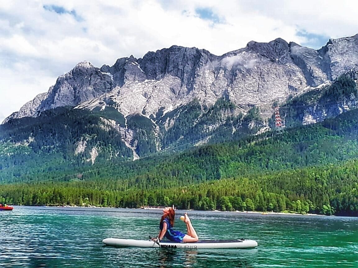 A person on a paddleboard in a lake with mountains in the background.