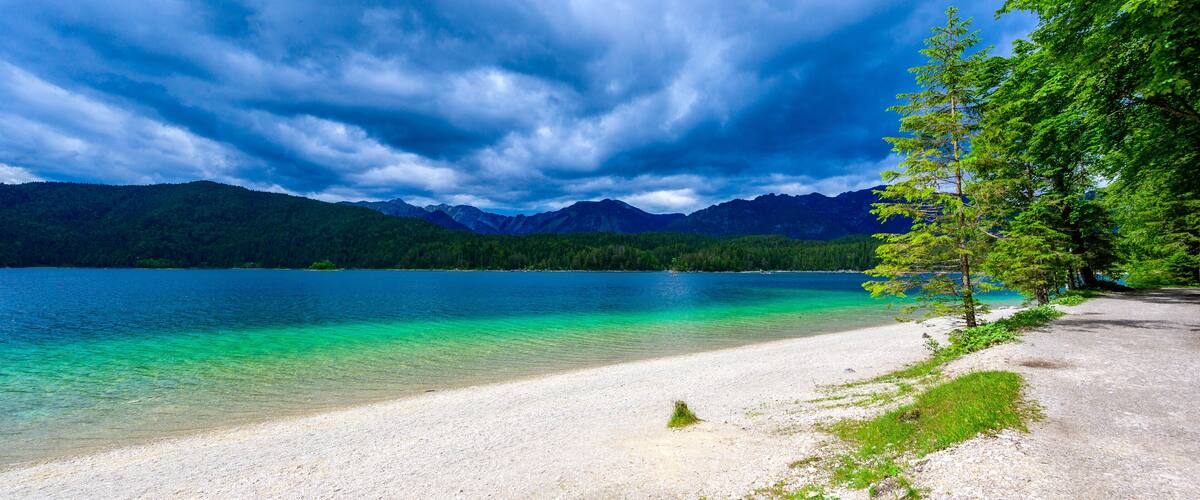 A lake with clear turquoise water, surrounded by mountains and a forested area.