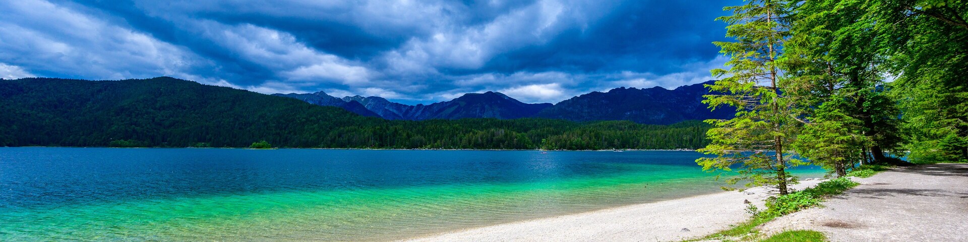 A lake with clear turquoise water, surrounded by mountains and a forested area.