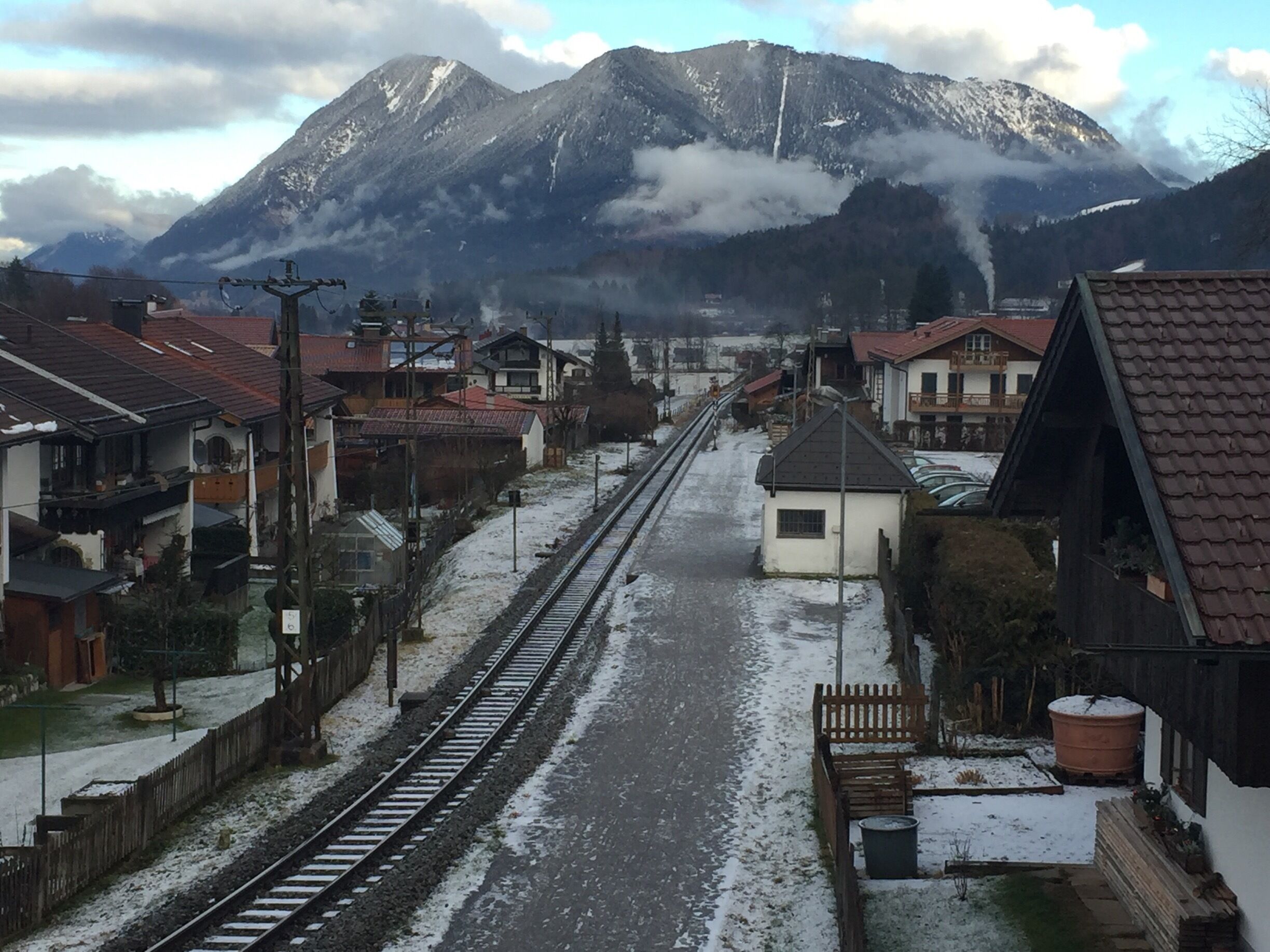A snow-covered railway track with houses and mountains in the background.