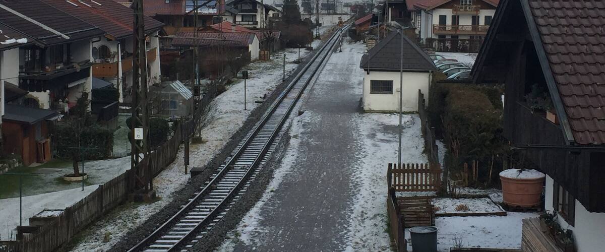 A snow-covered railway track with houses and mountains in the background.