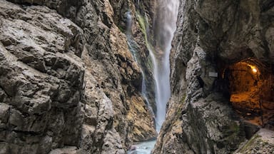 A waterfall in a rocky gorge with a cave entrance.