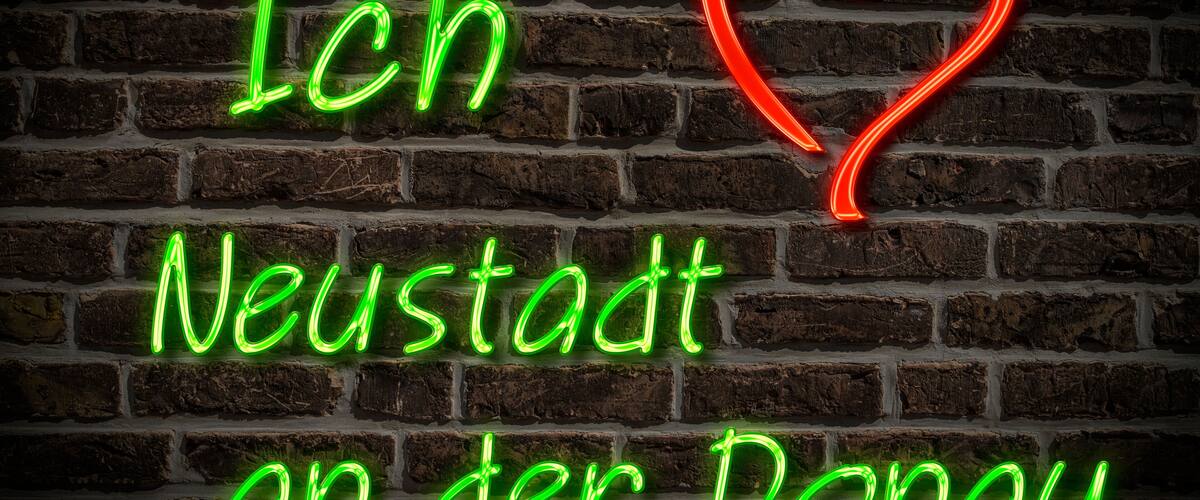 A neon sign with the text 'Ich Neustadt an der Donau' on a brick wall.