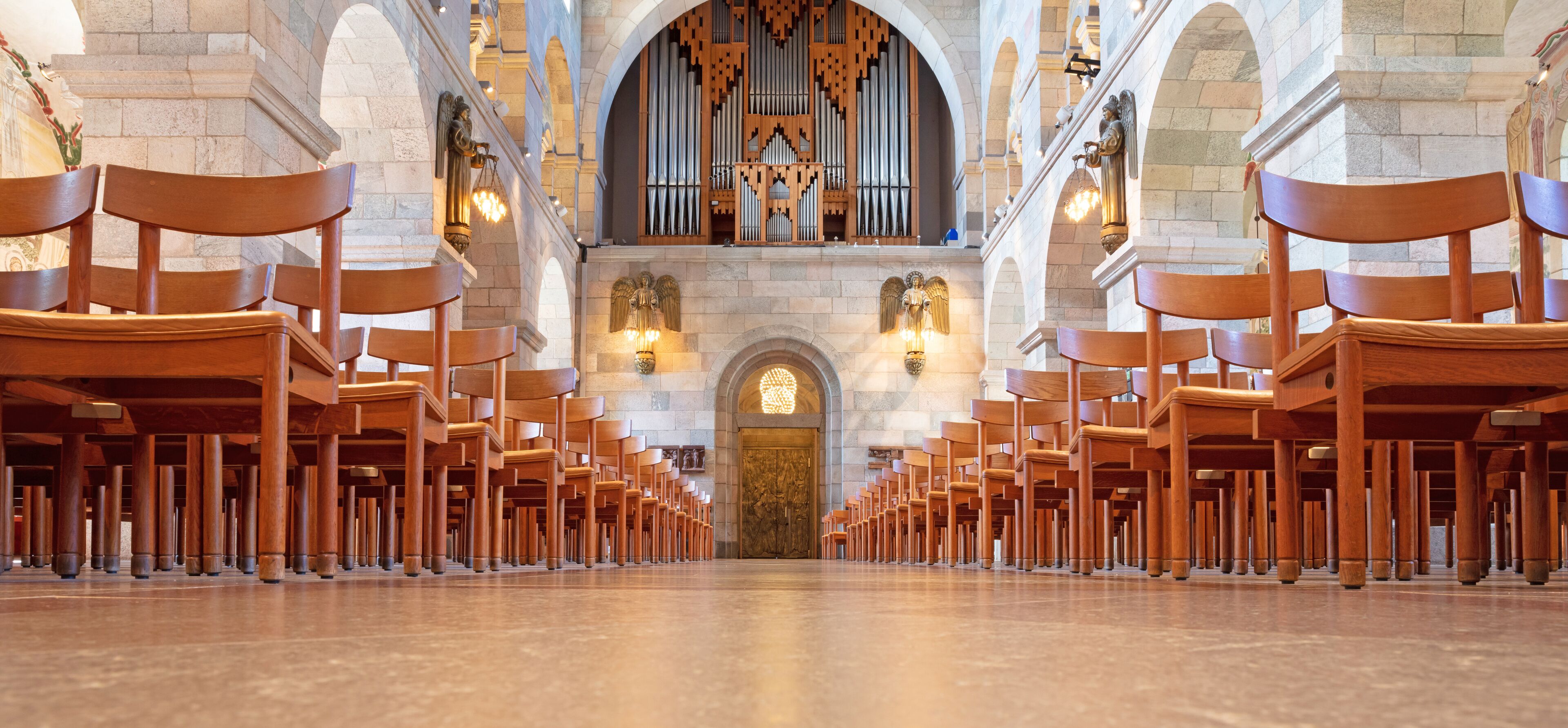 A church interior with rows of wooden pews, a large organ, and stone arches.