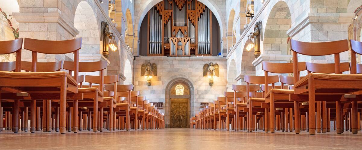 A church interior with rows of wooden pews, a large organ, and stone arches.