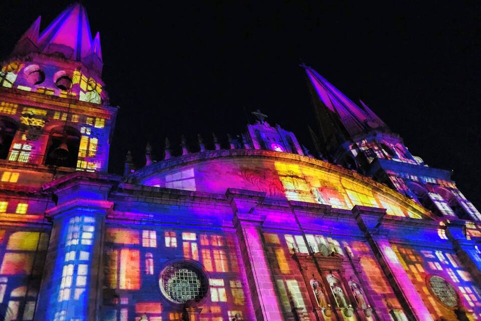Un bâtiment historique aux couleurs vives, illuminé de teintes éclatantes, avec une tour de l’horloge et des flèches.