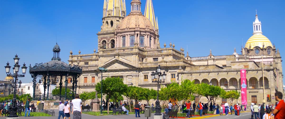 A historic cathedral with multiple spires and a large dome, surrounded by a public square with people and trees.
