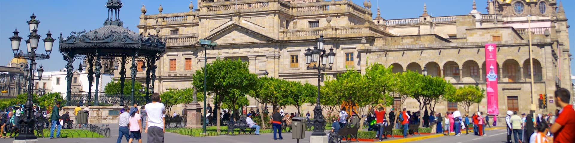 A historic cathedral with multiple spires and a large dome, surrounded by a public square with people and trees.