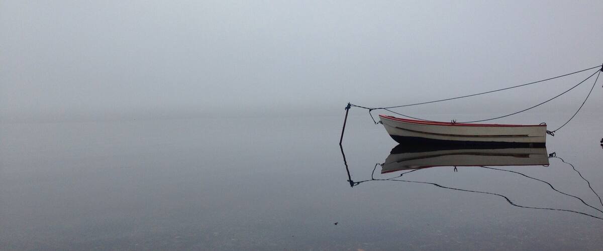 A small boat tied to a dock with calm water and overcast sky.