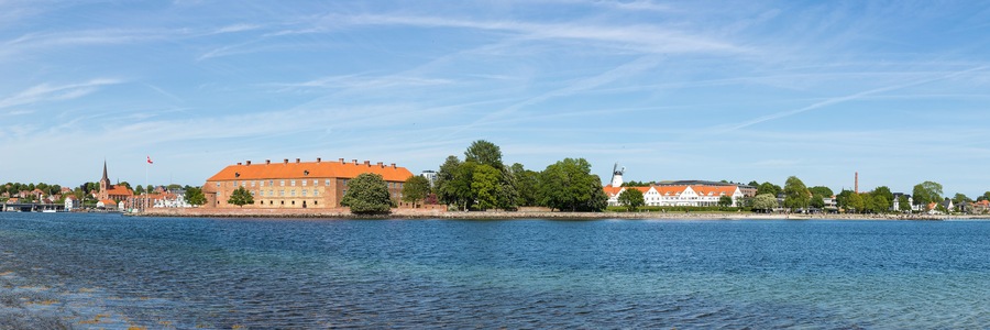 A river with a large building with an orange roof and a church with a tall spire.