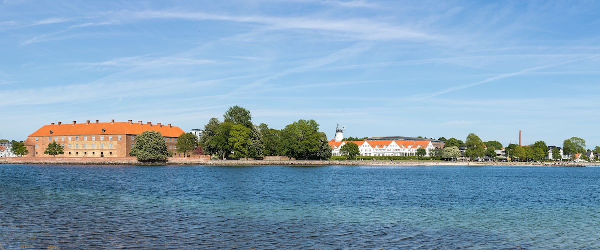 A river with a large building with an orange roof and a church with a tall spire.