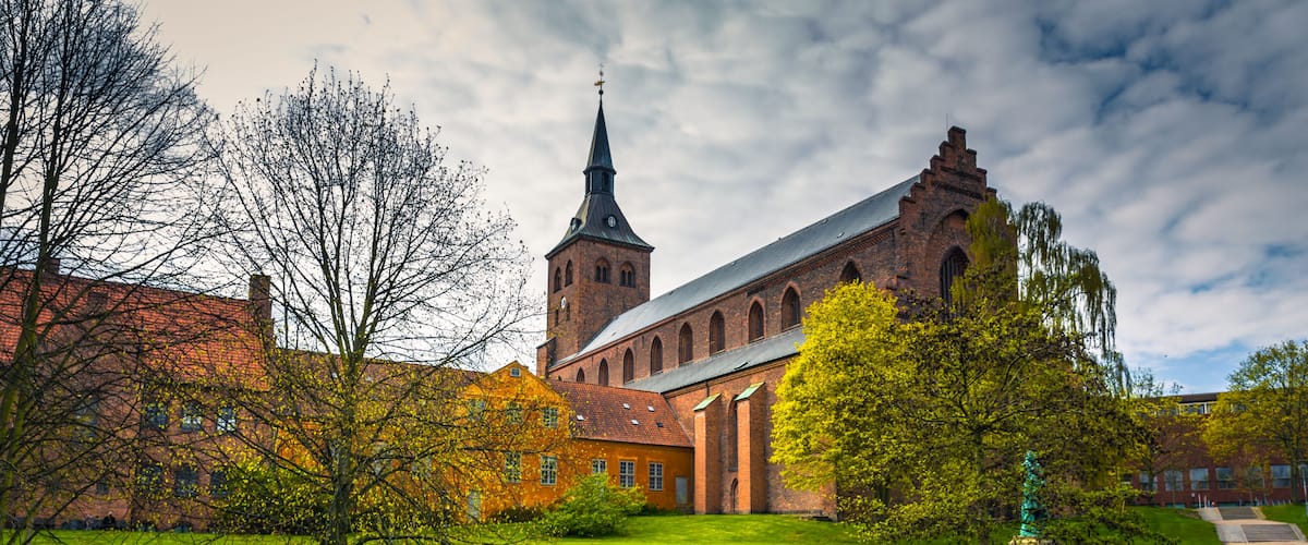 A historic church with a tall tower, a pond, and a well-maintained lawn.