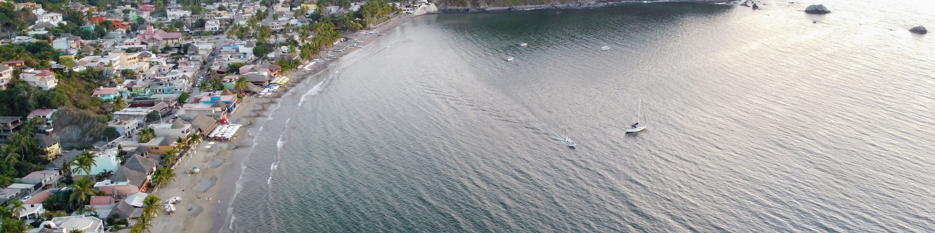 Un pueblo costero con playa, casas y una colina boscosa.