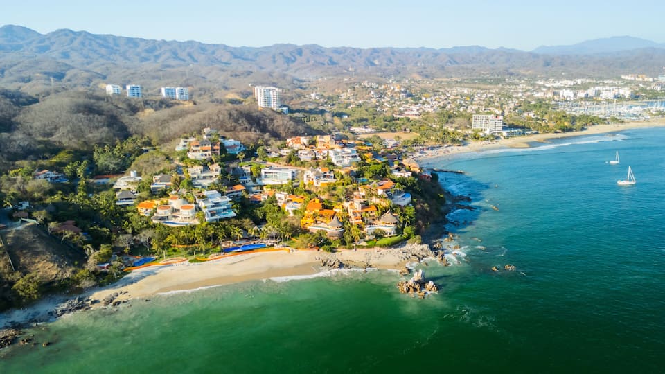 A coastal town with a beach, houses, and mountains in the background.