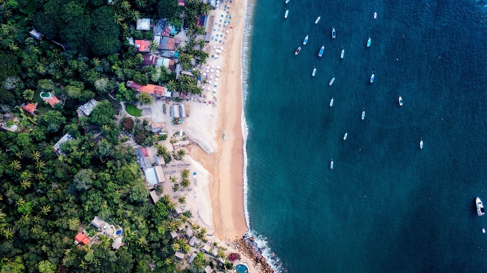 An aerial view of a beach with boats, palm trees, and buildings.