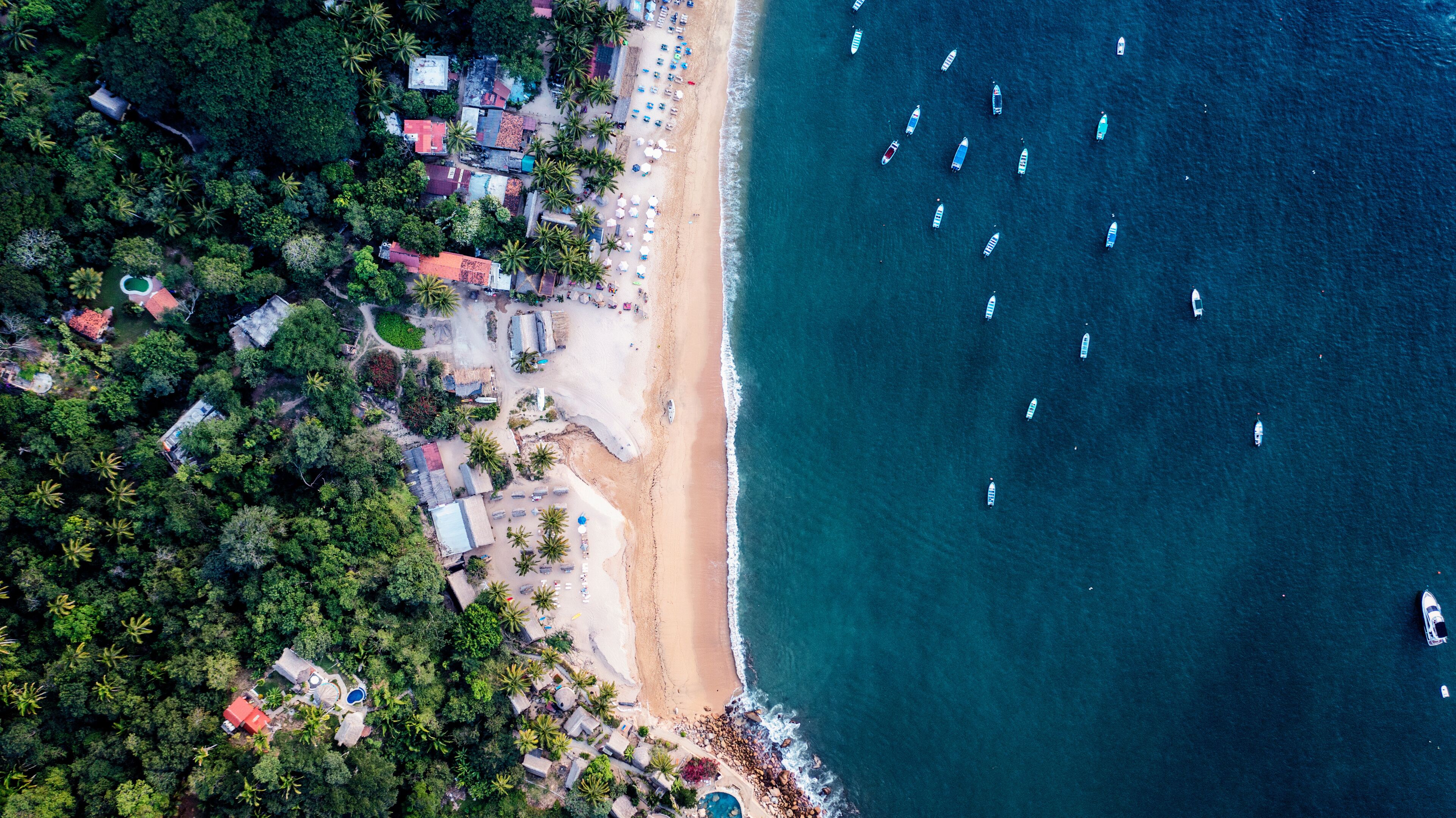 An aerial view of a beach with boats, palm trees, and buildings.
