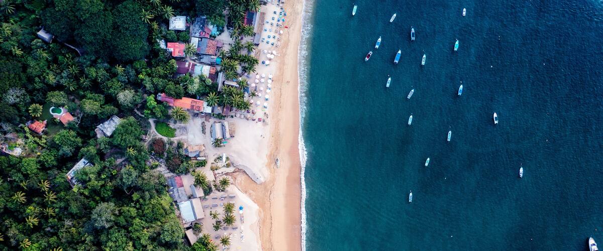 An aerial view of a beach with boats, palm trees, and buildings.