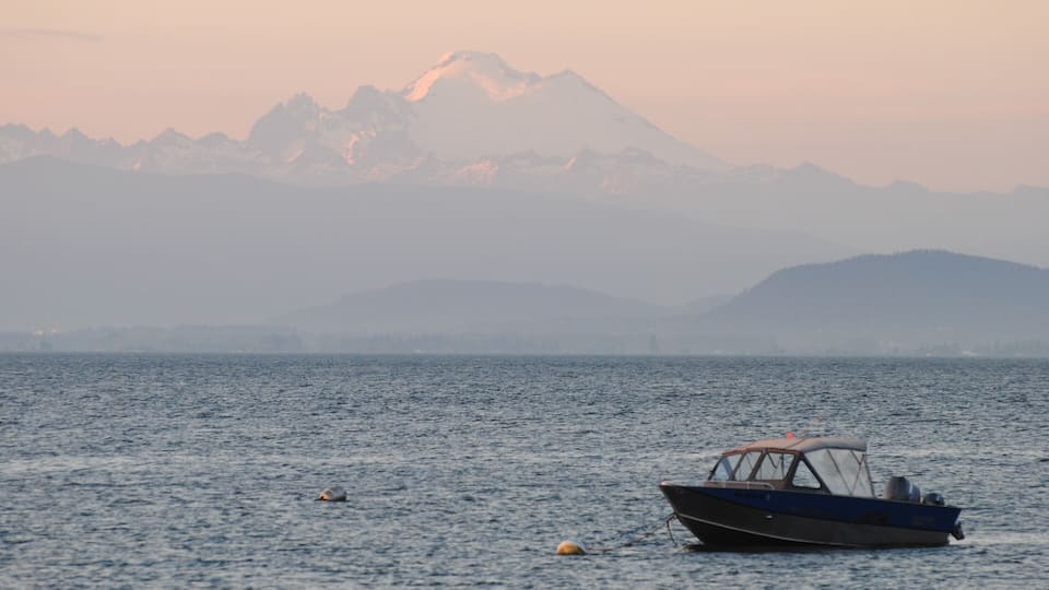 A boat on calm water with a mountain range in the background.