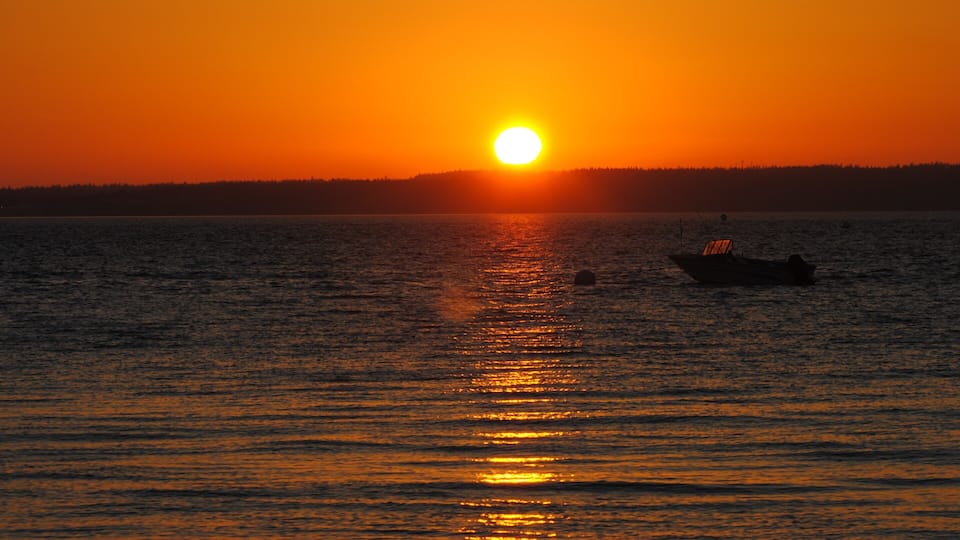 A sunset over a calm body of water with a boat and a forested shoreline.