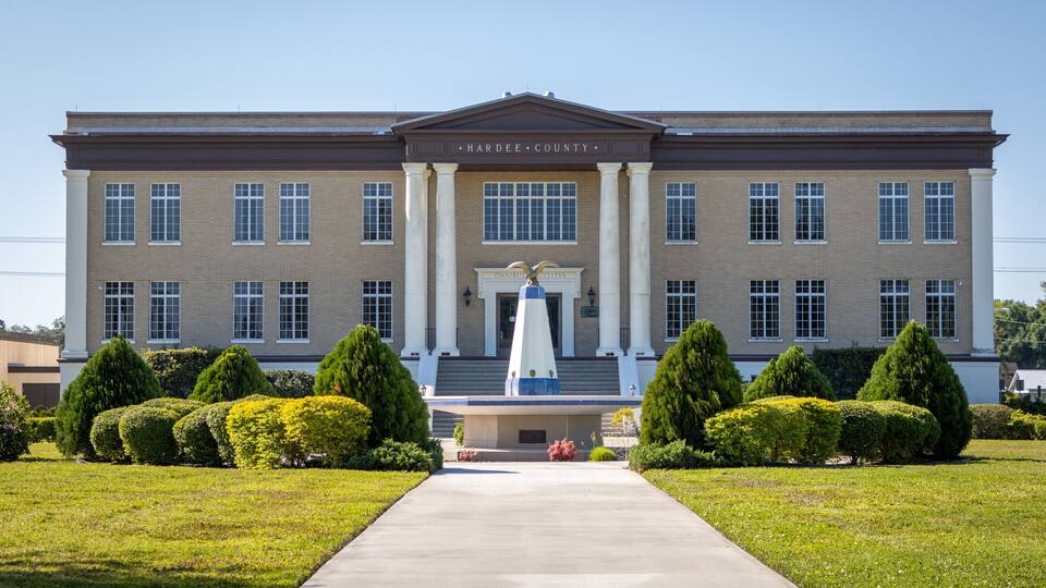 A large brick courthouse with a central entrance and a statue in front.