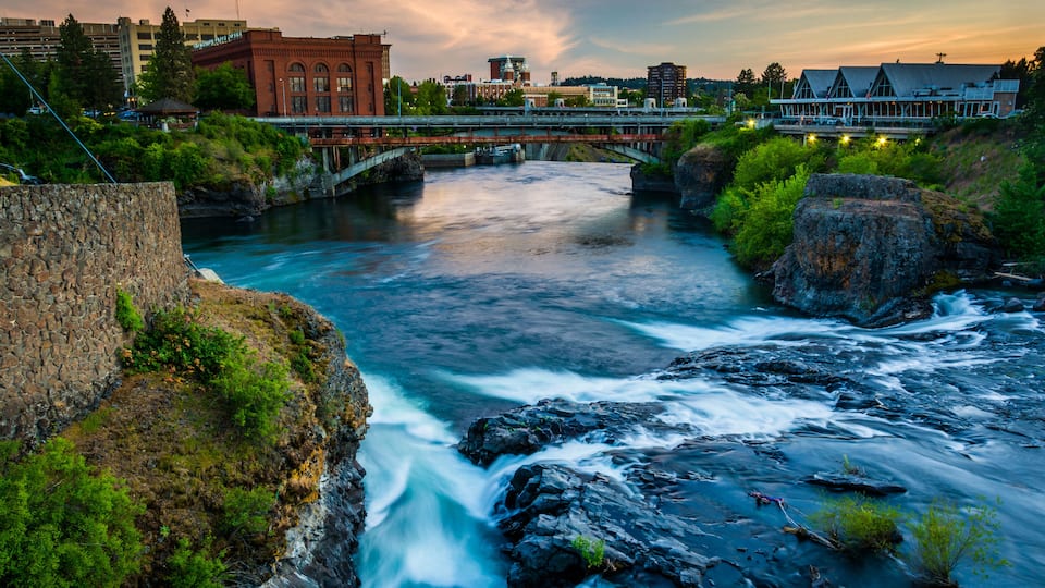 A river flowing through a rocky landscape with a bridge and buildings in the background.