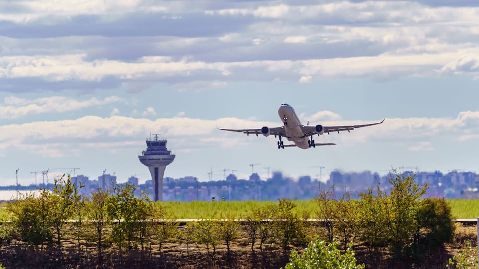 An airplane taking off with a control tower and a green landscape in the background.