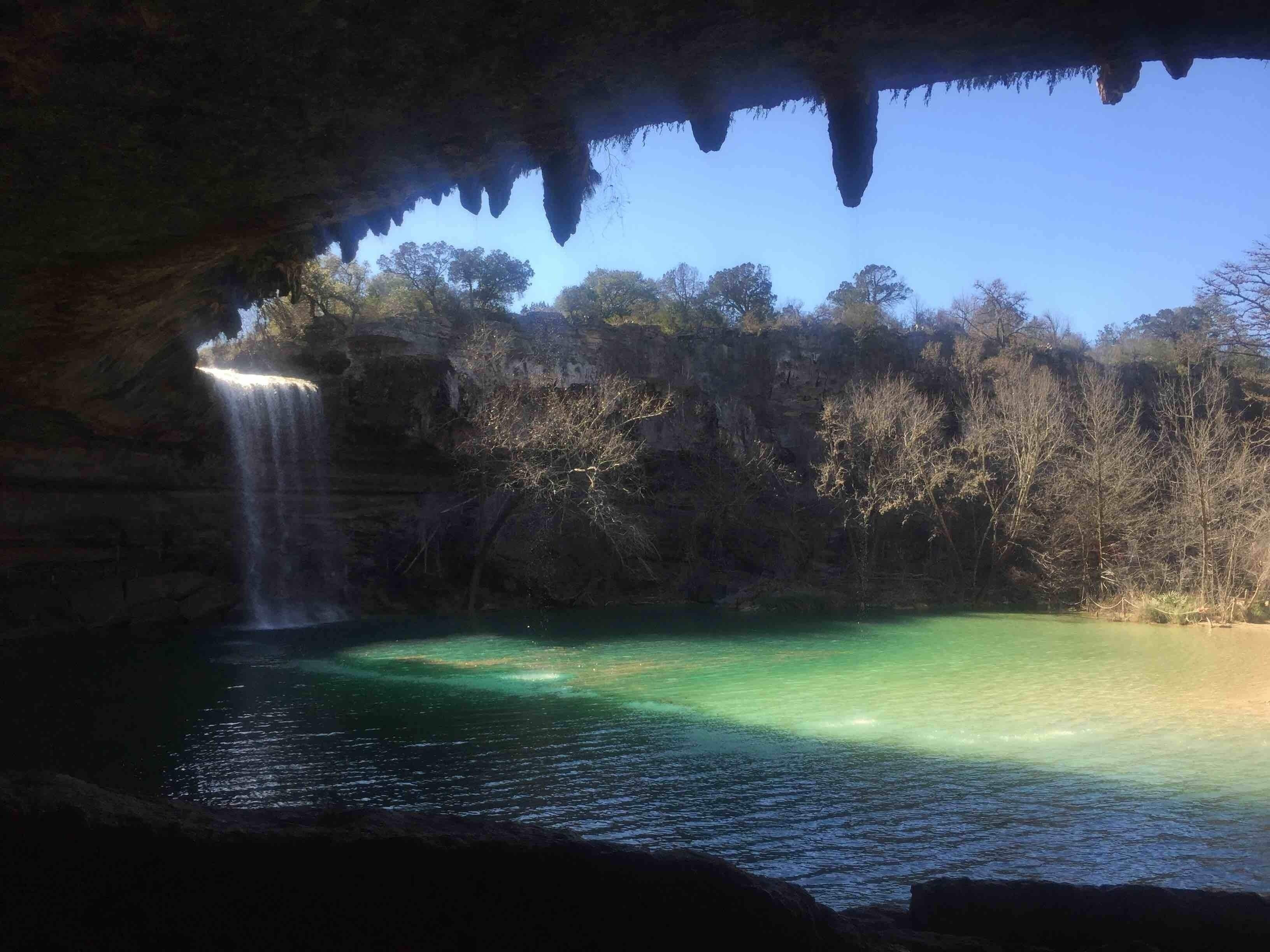 A waterfall cascading into a clear pool surrounded by forested cliffs.