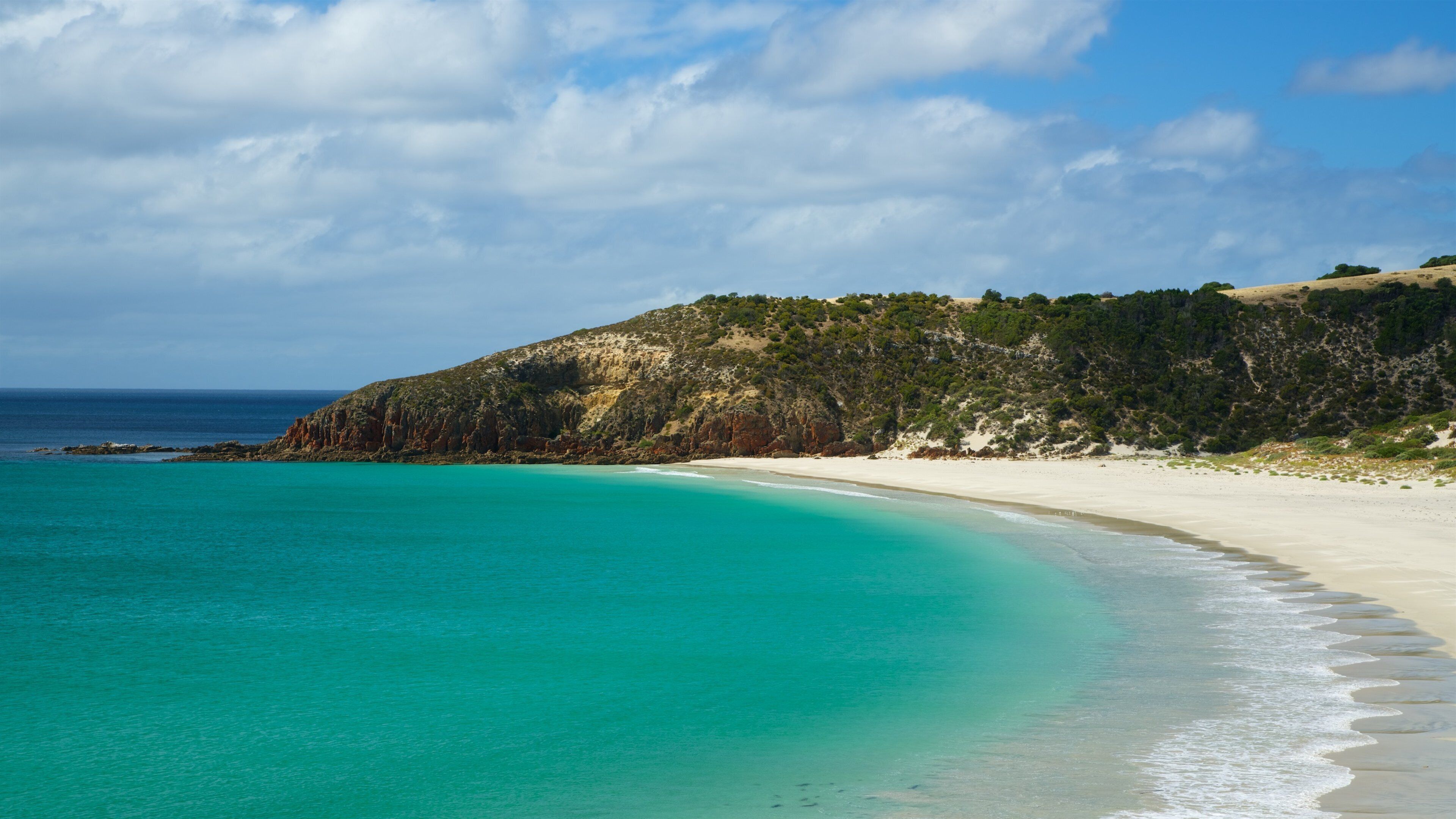 A turquoise beach with white sand, a rocky cliff, and a clear blue sky.