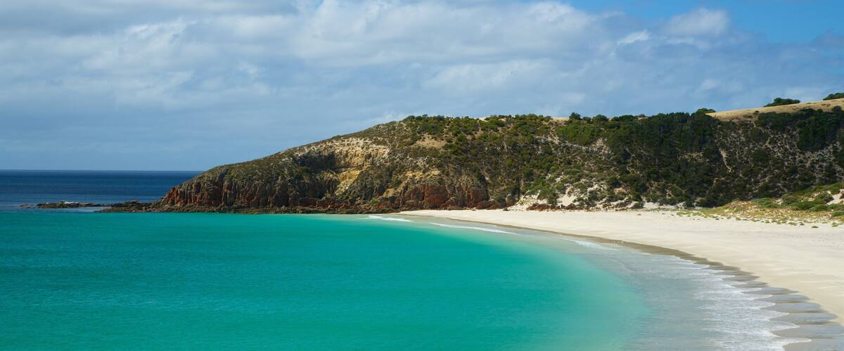 A turquoise beach with white sand, a rocky cliff, and a clear blue sky.